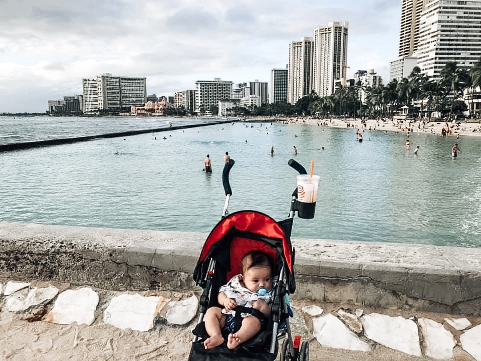 Baby in red stroller in front of water in Hawaii