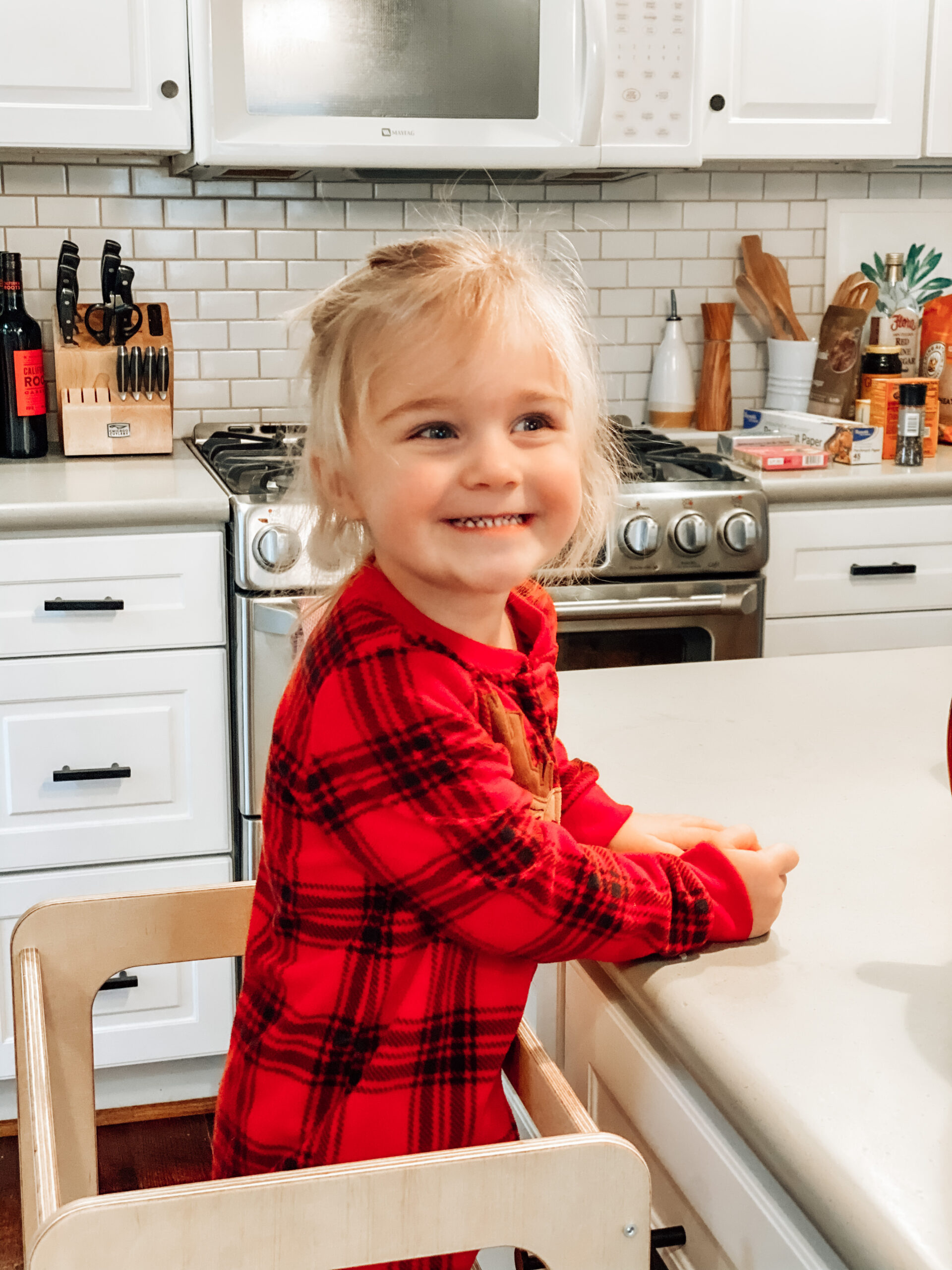 Toddler standing at a learning tower in red plaid pajamas